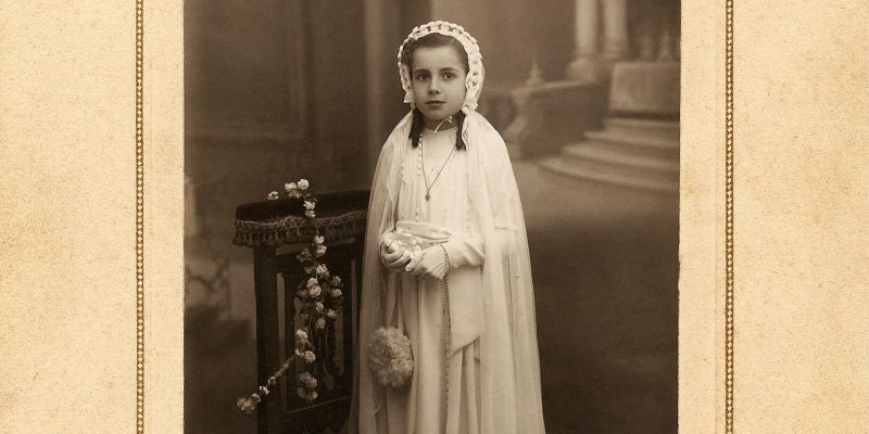 Retrat de primera comunió de Joana Soteras al conegut estudi fotogràfic Vilardell. La fotografia és d’un cop acabada la guerra, no obstant, el cartró és antic: hi figura, en català, l’adreça amb el nomenclàtor de la República. 